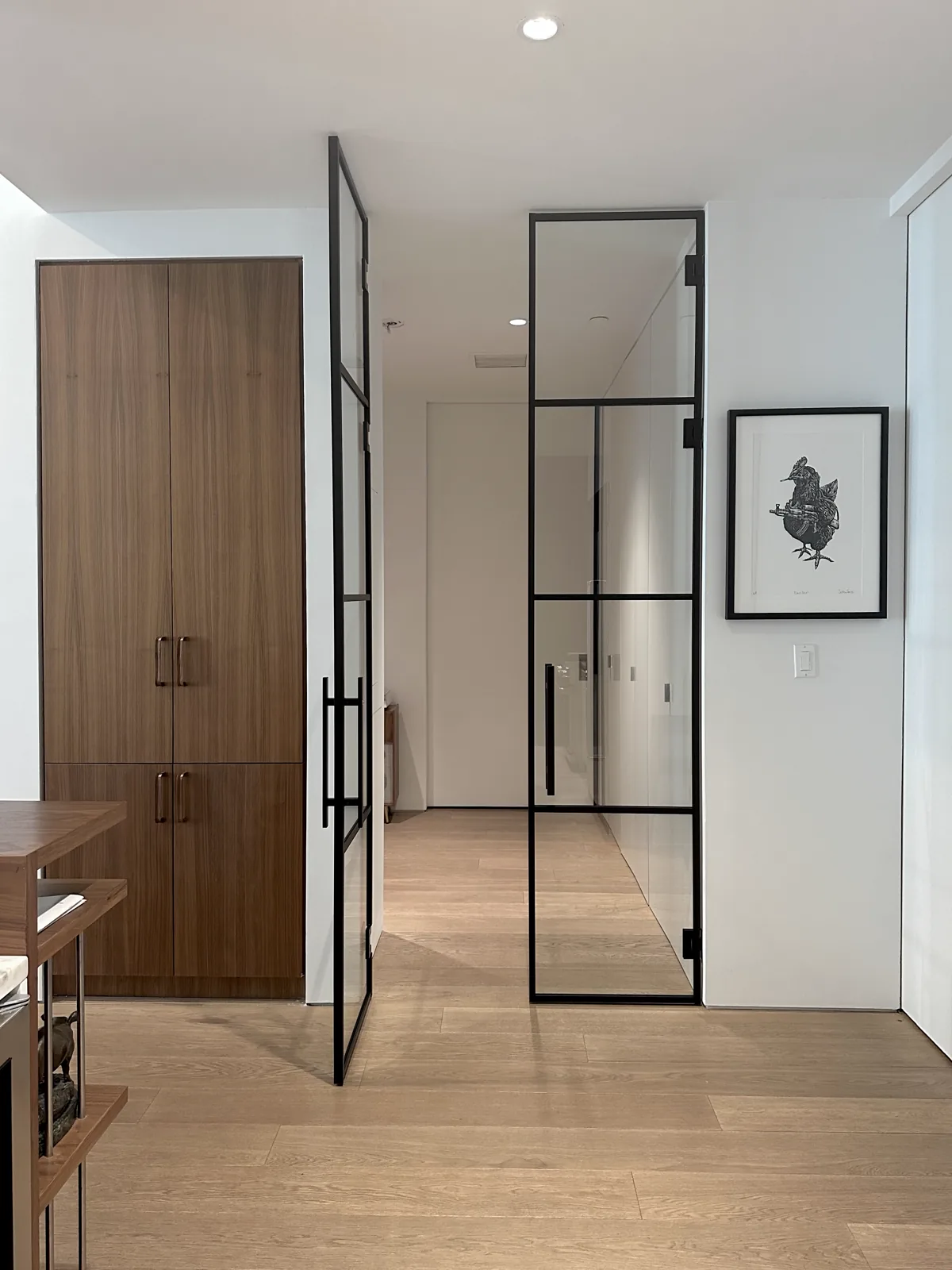 Slim black framed pivot glass door open between a kitchen and hallway